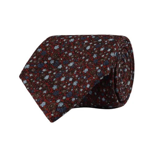 The AMANDA CHRISTENSEN - FLORAL WOOL TIE IN RUST MELANGE is a rolled-up tie in a rich rust melange hue, adorned with a subtle floral motif and delicate blue and white dots, showcased on a white background—an elegant selection from AMANDA CHRISTENSEN’s luxury men’s accessories.
