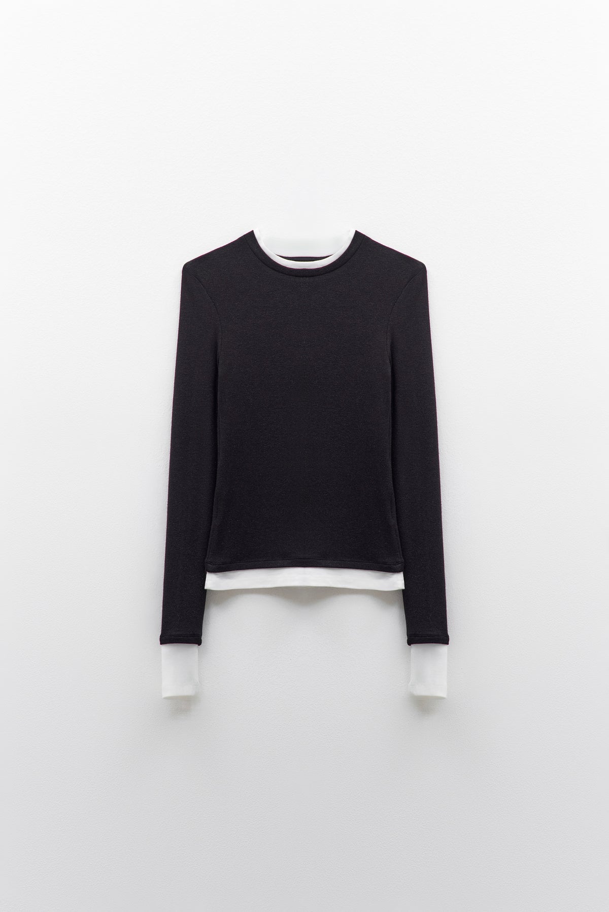 The ELEH - THE CONTRAST LAYER TOP by ELEH is a modern black long-sleeved sweater with white trim on the collar, cuffs, and hem—an effortlessly versatile wardrobe essential shown flat against a white background.