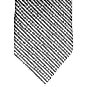 A rolled-up COLLARED GREENS - SIGNATURE STRIPE TIE IN BLACK by BIRD DOG BAY, handmade in New York from luxurious woven silk, featuring black and white diagonal stripes displayed against a white background.