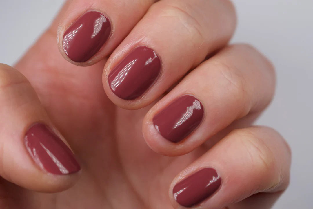 A glass bottle of TENOVERTEN - NAIL POLISH from the brand TEN OVER TEN, featuring a white cap and a dusty pink nail color. The front label displays "TEN OVER TEN" in white uppercase letters. This vegan, eight-free formula ensures both beauty and peace of mind. The background is plain and light-colored.
