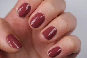 A glass bottle of TENOVERTEN - NAIL POLISH from the brand TEN OVER TEN, featuring a white cap and a dusty pink nail color. The front label displays "TEN OVER TEN" in white uppercase letters. This vegan, eight-free formula ensures both beauty and peace of mind. The background is plain and light-colored.