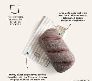 The LAMBWOLF COLLECTIVE - RYE DOG TOY by LAMBWOLF COLLECTIVE is a plush toy shaped like a loaf of bread with three slits on top, cleverly designed as a treat-hiding toy, and shown here resting on a beige and white striped cloth.