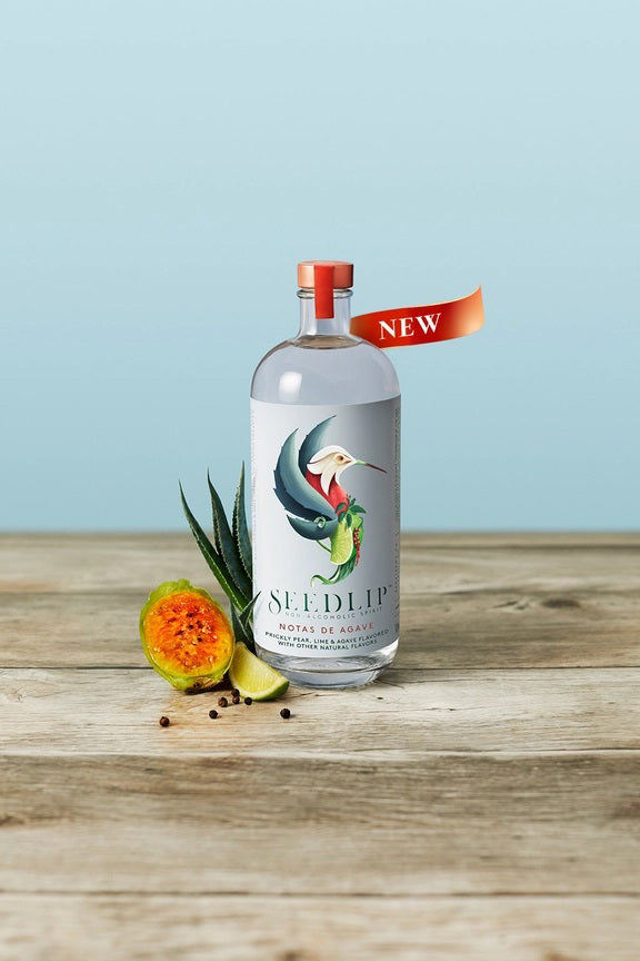 SEEDLIP - NOTAS DE AGAVE NON ALCOHOLIC SPIRIT by SEEDLIP DRINKS comes in a clear bottle with a copper cap and a vibrant bird and fruit label on a light blue background—an ideal non-alcoholic option.