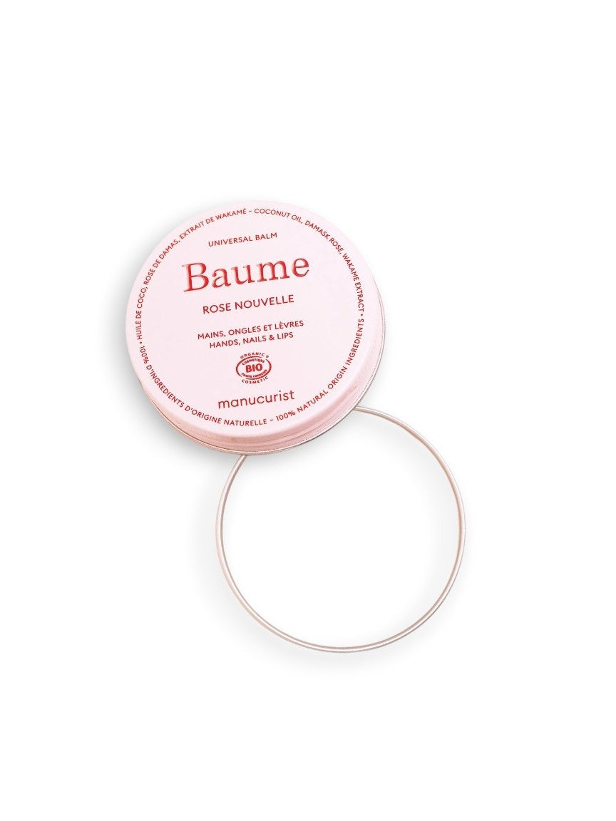 With red nails, a person with medium-dark skin applies MANICURIST - ROSE BALM COSMOS ORGANIC NATURAL NOURISHING BALM by MANUCURIST INC to the back of their left hand against a light pink background. Perfect for lips, nails, and cuticles.