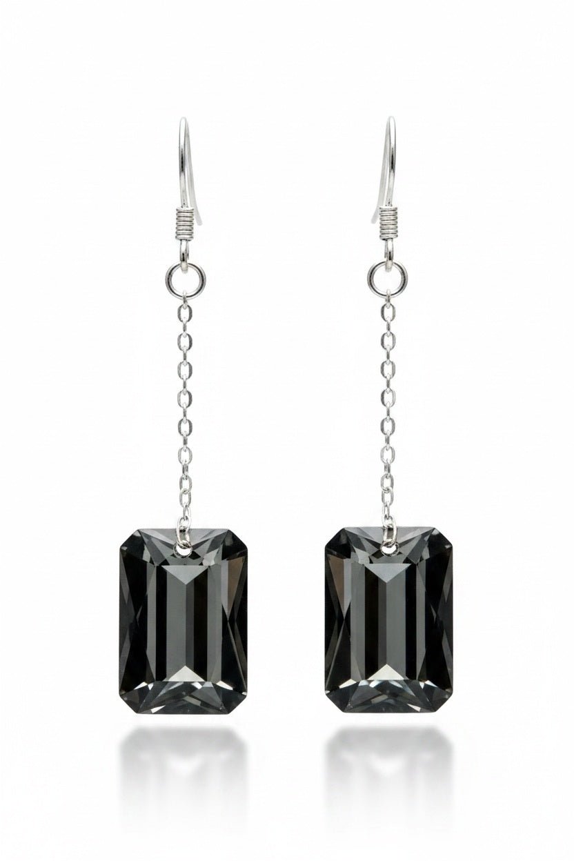 Introducing the VERDIER - SWAROVSKI NIGHT CRYSTAL EARRINGS by VERDIER: a pair of sterling silver drop earrings featuring rectangular, emerald-cut Swarovski crystals suspended from delicate chains, beautifully showcased against a white background.