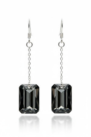 Introducing the VERDIER - SWAROVSKI NIGHT CRYSTAL EARRINGS by VERDIER: a pair of sterling silver drop earrings featuring rectangular, emerald-cut Swarovski crystals suspended from delicate chains, beautifully showcased against a white background.