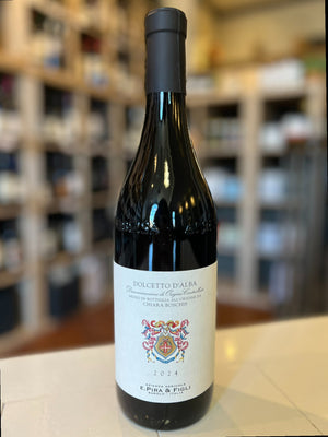 A bottle of WINE: GRAPEVINE E. PIRA DOLCETTO D'ALBA 2024 red wine, with a cream label showing a crest and text, is displayed against a plain white background.