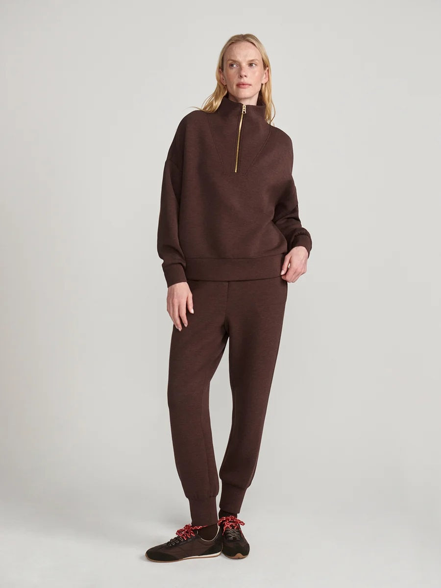 A person wears an oversized, dark brown VARLEY - HAWLEY HALF-ZIP SWEATSHIRT IN COFFEE BEAN MARL with a gold zipper.