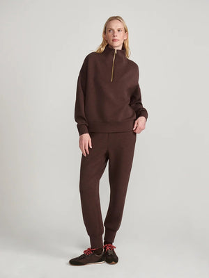 A person wears an oversized, dark brown VARLEY - HAWLEY HALF-ZIP SWEATSHIRT IN COFFEE BEAN MARL with a gold zipper.