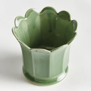 The NAPA HOME AND GARDEN - Maline Footed Pot in Green (Small) is a light green ceramic pot featuring scalloped edges and vertical panels, perched on a small round base, set against a plain white background.