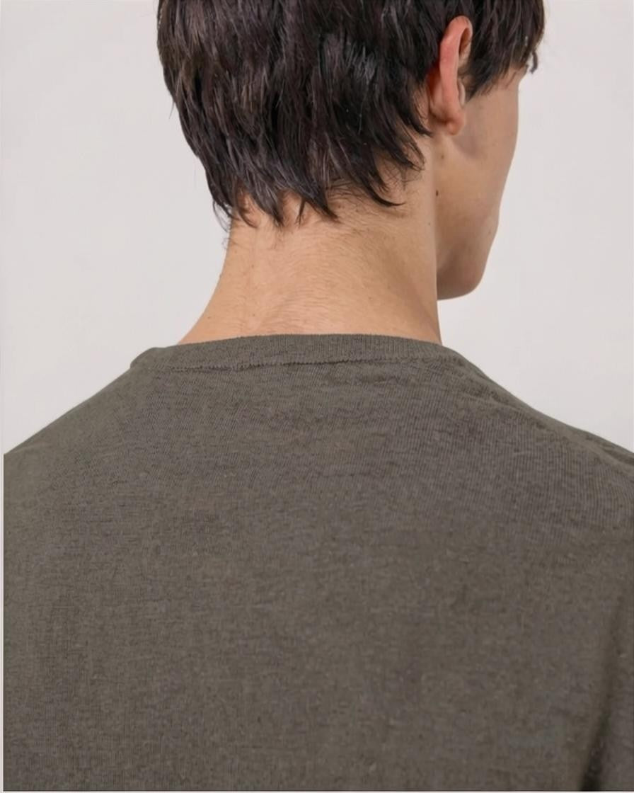 A young person with short dark hair is wearing the HARTFORD - EXTRA-FINE MERINO WOOL CREW PULLOVER IN MUSHROOM, standing against a light background and looking at the camera with a neutral expression, one arm crossed.