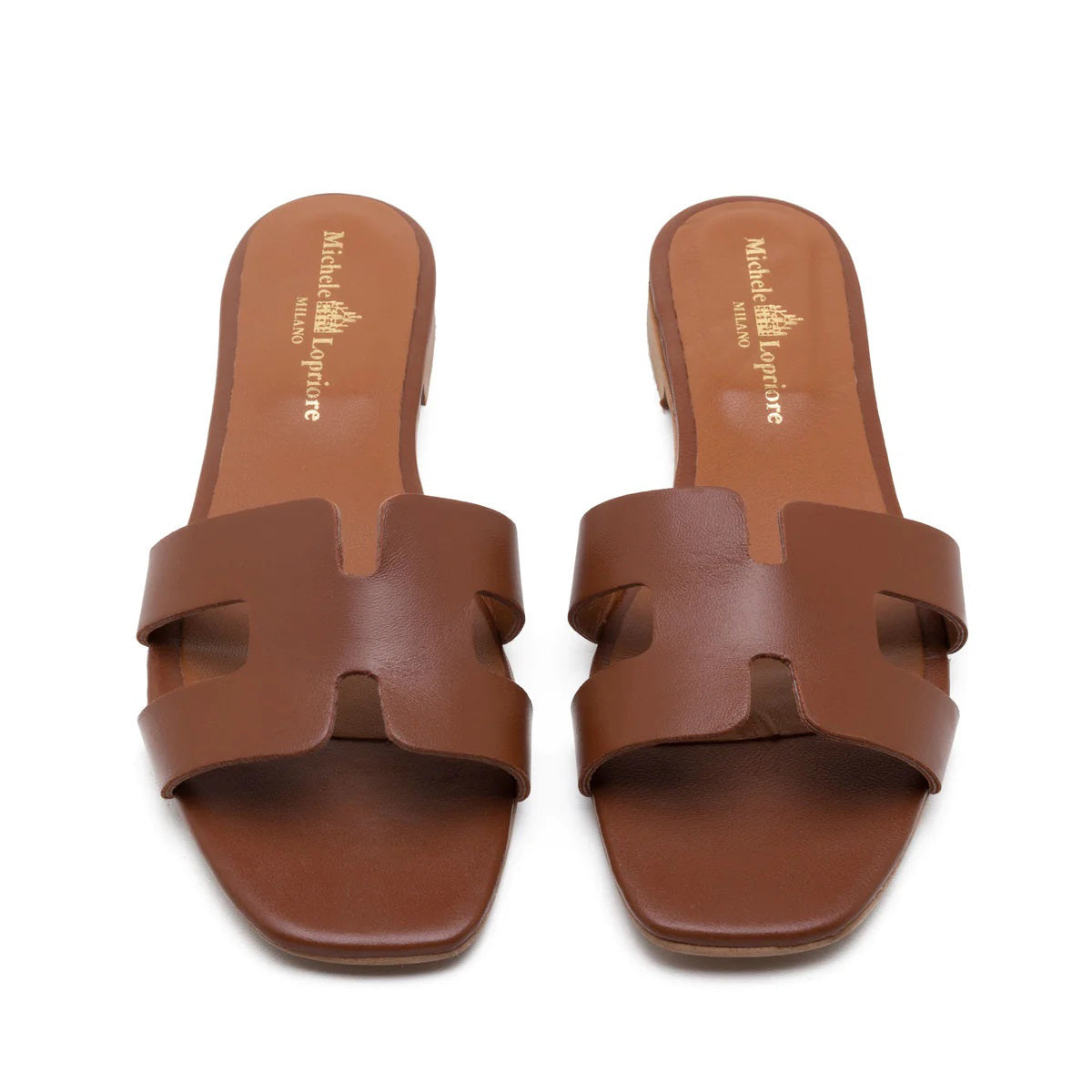 The image depicts the MICHELE LOPRIORE - H SLIDE, a single brown leather slide sandal with an open-toe design. The upper features two wide straps with geometric cutouts. The thin sole appears to be made of light brown wood-like material. Made in Italy by MICHELE LOPRIORE, the sandal is displayed against a plain white background.