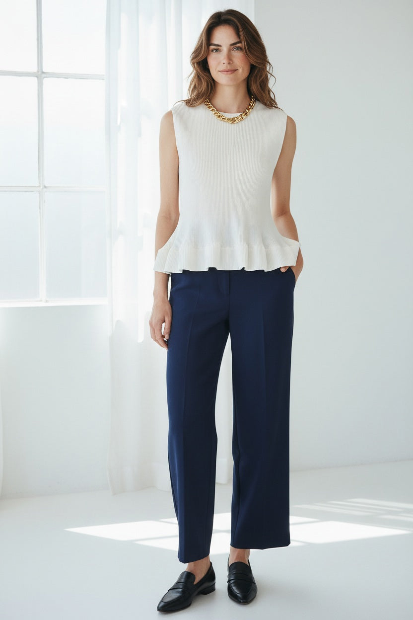 A person wears the MEIMEIJ - PLEATED SLEEVELESS TOP by MEIMEIJ with a silver chain necklace and a vibrant floral skirt, set against a plain white background—a chic choice to pair with summer trousers for effortless style.