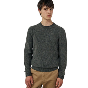 A young man with short dark hair wears the HARTFORD Seamless Wool Crew Pullover in Camo Green and tan pants, standing against a plain light-colored background, looking slightly to the side with a neutral expression.