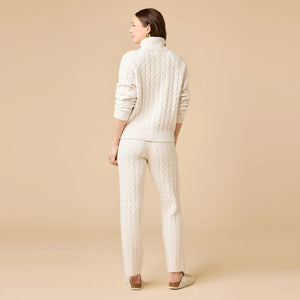 A woman wearing a marshmallow-soft, cream-colored SOFTIES - CABLE KNIT MARSHMALLOW ½ ZIP WITH TAPERED PANT SET, featuring a half-zip pullover and matching pants with a drawstring waist.
