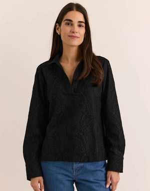 A woman wearing a HINSON WU - MONA LONG SLEEVE BONDED LACE SHIRT in black, paired with black trousers, black heels, and a black clutch.