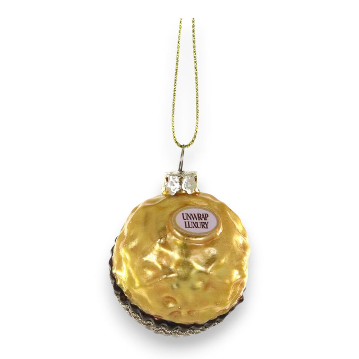 The CHOCOLATE HAZELNUT BON BON ORNAMENT by CODY FOSTER is a glass Christmas tree ornament shaped like a gold foil-wrapped candy with a &quot;UNWRAP LUXURY&quot; label, hanging by a gold string.