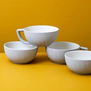 Four BE HOME - CROSSHATCH LATTE MUGS by BE HOME, INC, including one with a handle, are stacked against a yellow background—ideal for sustainable breakfasts and supporting women-owned artisan brands.