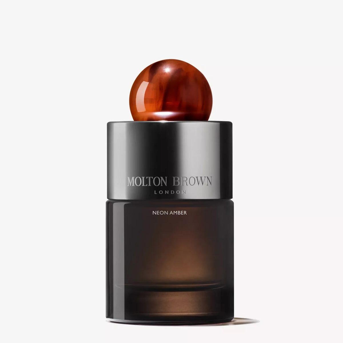 A 100ml bottle of MOLTON BROWN - NEON AMBER EAU DE PARFUM, featuring a dark translucent base, metallic silver band, and shiny amber spherical cap, displayed against a plain white background.