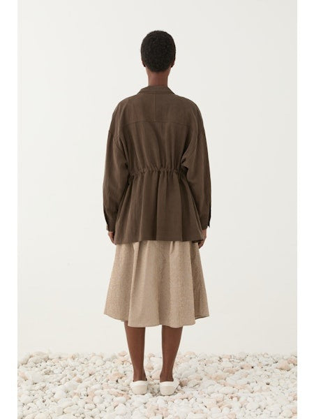 Someone wears the ELEH - JACKET WITH TIE WAIST by ELEH over a white t-shirt and a light beige textured skirt, standing against a plain light background.
