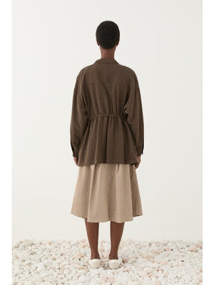 Someone wears the ELEH - JACKET WITH TIE WAIST by ELEH over a white t-shirt and a light beige textured skirt, standing against a plain light background.
