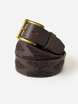The LA MATERA - CASTANO POLO BELT by LA MATERA, featuring a dark brown leather embossed geometric design and brass buckle, is handcrafted in Argentina and coiled neatly against a plain white background.