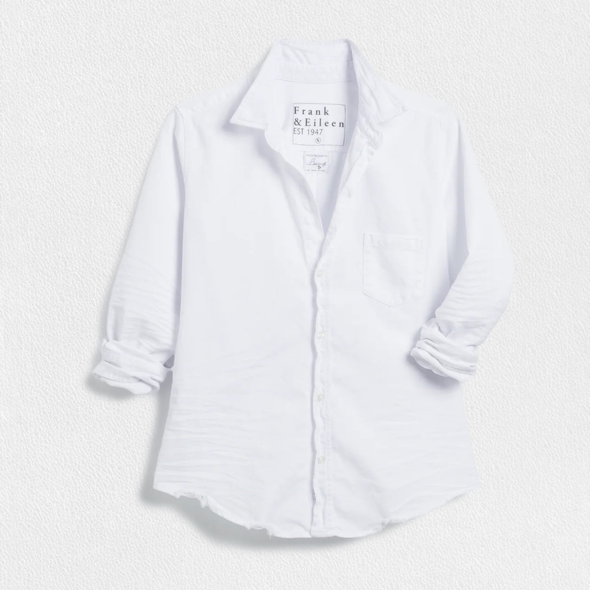 A white, long-sleeved button-up shirt with a pocket on the left chest. The shirt features a collar and casually rolled-up sleeves. This foundational piece, the &quot;FRANK AND EILEEN - BARRY TAILORED BUTTON UP IN FAMOUSE DENIM WHITE&quot; by FRANK &amp; EILEEN, exudes classic style against a white textured background.