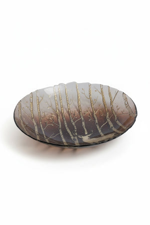 ZODAX WILDERNESS SERVING BOWL IN TAUPE AND GOLD 13″, a round glass serving bowl with a translucent taupe gradient featuring an etched pattern of trees and a deer silhouette in gold.