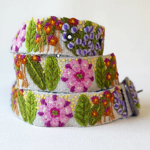 A person wears a magenta long-sleeve top, dark blue jeans, and the JENNY KRAUSS - FRESHWATER BELT by JENNY KRAUSS, handcrafted in Peru and adorned with colorful embroidered flowers and leaves.