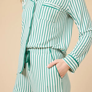A woman wears the SOFTIES ARIA SLIM NOTCH COLLAR PJ SET, featuring a long-sleeved button-down top and matching wide-leg pants in red and white vertical stripes with red piping details.