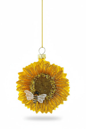 The CODY FOSTER SUNFLOWER WITH BEE ORNAMENT features gold glitter accents and a charming bee, making it an ideal collector’s piece or gift for design lovers, displayed hanging by a gold string against a white background.