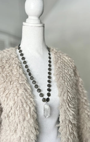 The ANN LIGHTFOOT Quartz and Smokey Glass Disc Pendant Necklace showcases round, dark smokey glass beads paired with a striking clear quartz pendant. Elegantly displayed on a white background, this 30-inch necklace by ANN LIGHTFOOT blends refined sophistication with natural allure.