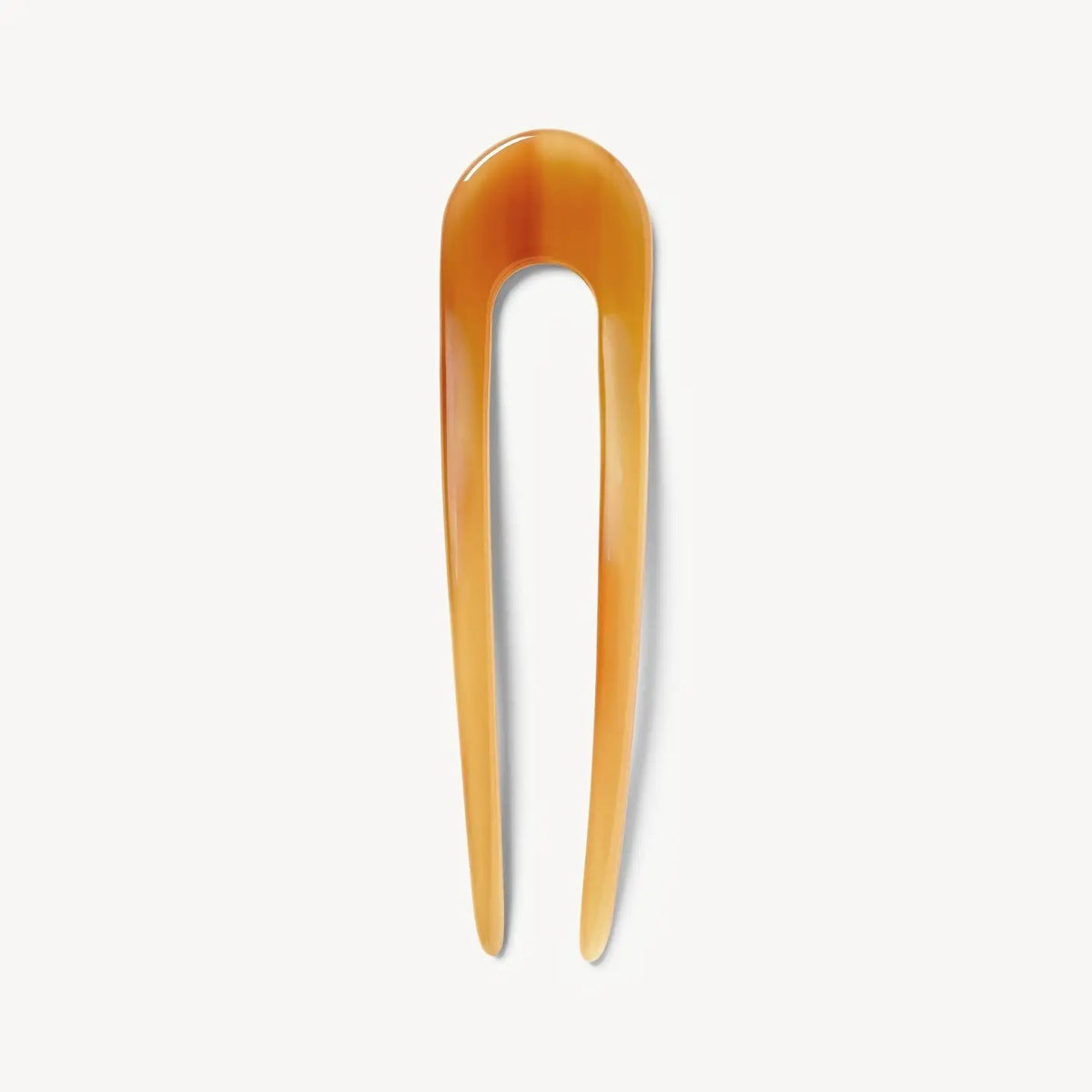 The MACHETE - FRENCH HAIR PIN IN COGNAC, a translucent amber two-prong hair fork handcrafted from Italian acetate, is displayed against a plain white background.