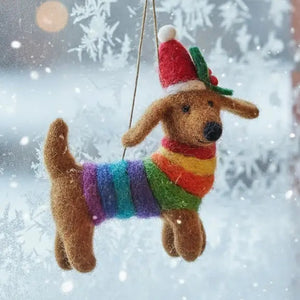 A FESTIVE RAINBOW PRIDE DOG ORNAMENT shaped like a needle felted dachshund wearing a rainbow-striped sweater, a Santa hat, and a holly sprig.