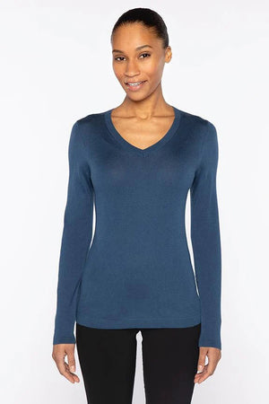 A woman with dark hair pulled back smiles in a KINROSS CASHMERE Fitted Vee Neck Silk Cashmere Sweater in blue and black pants, standing against a plain white background.