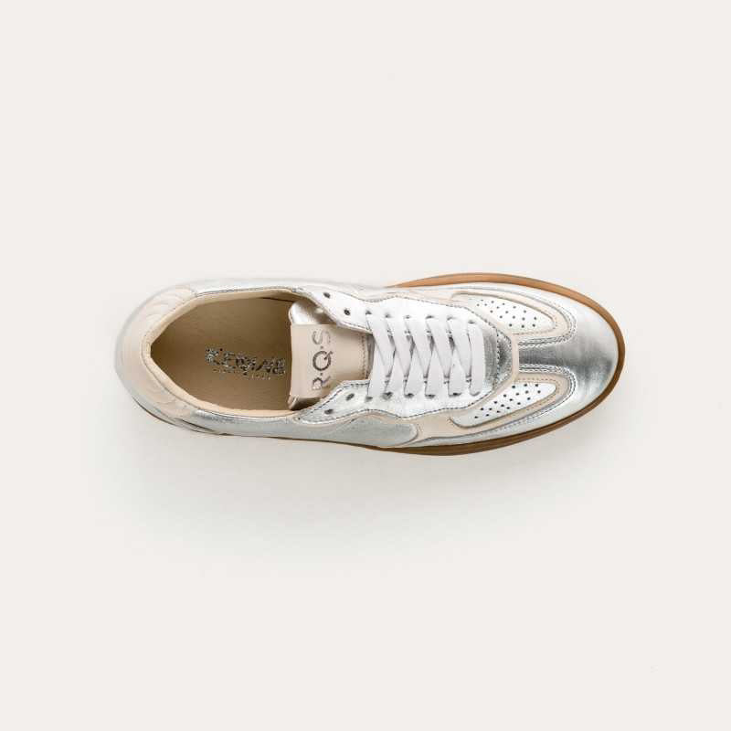 The REQINS - ATHENA METALLIC SNEAKER IN SILVER features a metallic silver finish, white laces, beige heel accents, suede leather details, and a brown rubber sole, displayed in side profile against a plain light background.