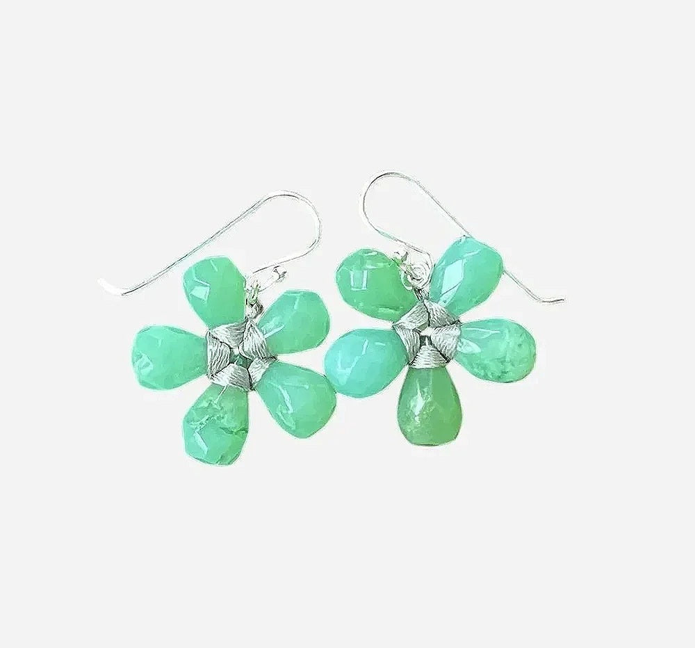 The ANN LIGHTFOOT - FACETED CHRYSOPRASE FLOWER EARRINGS by ANN LIGHTFOOT feature blossom-shaped designs crafted from five faceted green chrysoprase stones with delicate silver wire wrapping at the center, elegantly hanging from sterling silver hooks against a softly blurred, neutral background.