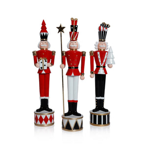 THE TWINKLE TROOP by ZODAX features individual 3.5" x 18" festive nutcracker figurines in red, black, and white, each on a patterned base, displayed among white ceramic cone-shaped trees against a red backdrop.