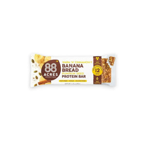 A protein bar wrapper labeled "88 ACRES - BANANA BREAD HIGH PROTEIN BAR" by 88 Acres. The wrapper highlights features such as "Nut-Free," "Vegan," "Gluten-Free," 12 grams of protein, and "No Palm Oil." The wrapper is set against a white wooden background.