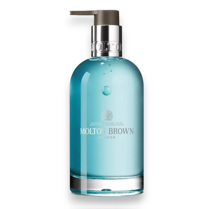 The MOLTON BROWN - COASTAL CYPRESS GLASS BOTTLE features fresh light blue hand wash in a clear bottle with a silver neck and gray pump, evoking marine notes, set against a white background.