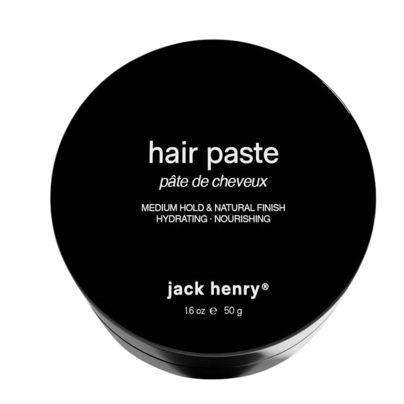 The black JACK HENRY - HAIR PASTE container features "pâte de cheveux" and “jack henry® 16 oz e 50 g” on the lid, offering medium hold, hydrating nourishment, and natural shine for healthy hair growth against a light background.