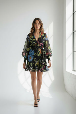 A close-up of the LAVI COUTURE - LIGEA FLORAL DRESS from LAVI highlights a vibrant botanical floral print with diverse flowers and green leaves on a black background. Bright oranges, pinks, blues, and greens add to the lively elegance of this exquisite Italian-made piece.