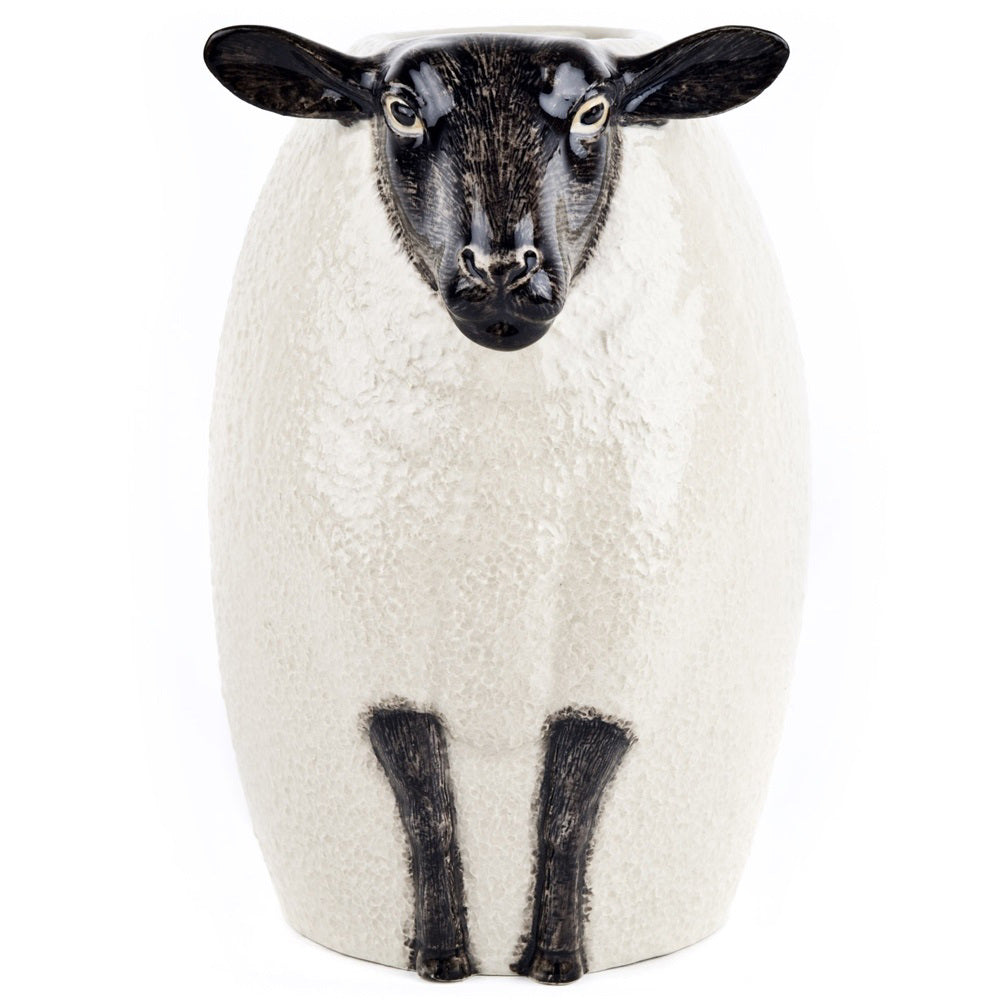 The QUAIL DESIGNS QUAIL CERAMICS - BLACK SUFFOLK SHEEP VASE, hand painted by artisans, displays a vibrant bouquet of white, purple, and maroon flowers with green foliage set against a white background.
