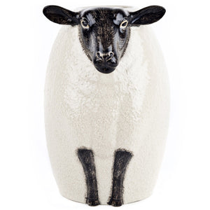 The QUAIL DESIGNS QUAIL CERAMICS - BLACK SUFFOLK SHEEP VASE, hand painted by artisans, displays a vibrant bouquet of white, purple, and maroon flowers with green foliage set against a white background.