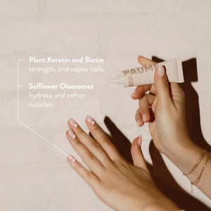 A tube of PAUME - ALL IN ONE CUTICLE AND NAIL CREAM by PAUME, infused with plant-based keratin, stands upright against a light beige background, showcasing minimal modern packaging in soft pink and white.