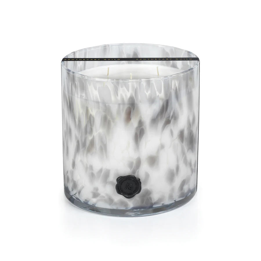 A large, cylindrical glass candle holder with a marbled black and white pattern, featuring five wicks at the top. A black wax seal logo is affixed to the front of the container. The candle within appears to be white and emits subtle hints of tarragon, lemon, and lavender when lit. This exquisite 5 WICK CANDLE by ZODAX is a perfect blend of elegance and aroma.