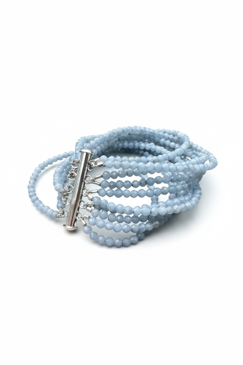 The ANN LIGHTFOOT - ANGELITE TEN STRAND BRACELET by ANN LIGHTFOOT features faceted light blue angelite beads strung across ten strands, secured with a silver slide clasp and displayed in a loose coil on a white background.