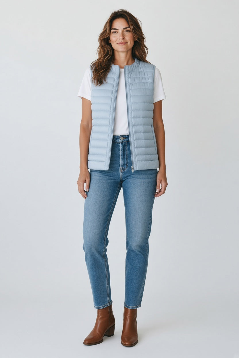 An older woman with short gray hair wears the SAVE THE DUCK - MARA PUFFER VEST over a white t-shirt and beige pants, standing against a light background—perfect for spring–summer layering from SAVE THE DUCK.
