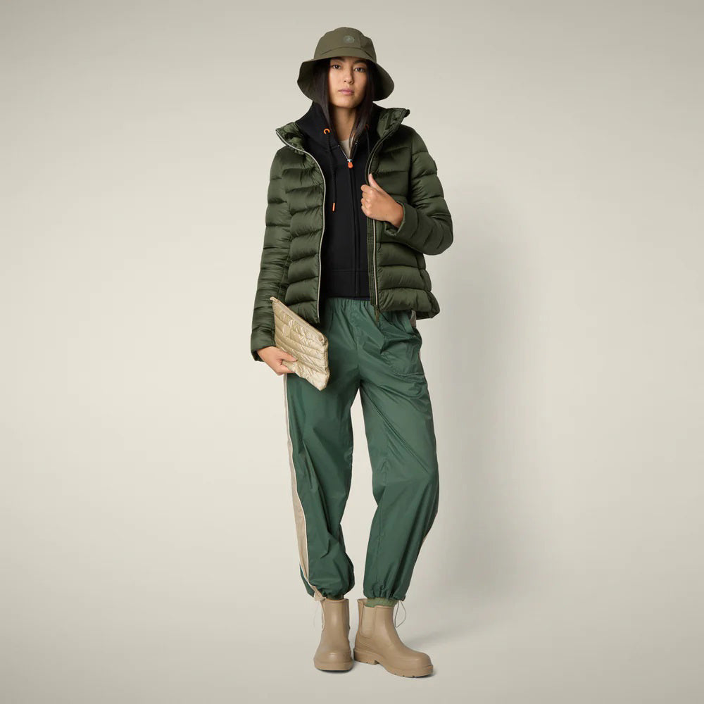 A person stands facing away in the SAVE THE DUCK - ELSIE PUFFER JACKET by SAVE THE DUCK, paired with loose green pants and tan boots against a plain light background.