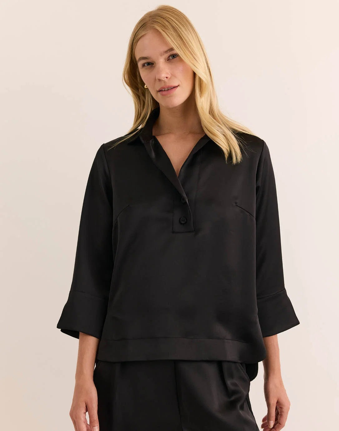 A woman with blonde hair models the HINSON WU Aileen 3/4 Sleeve Liquid Satin Shirt in black, featuring a collar and button details, against a plain light background.